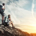 Two tourists with backpacks enjoying sunset on top of a mountain