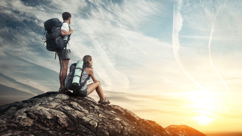 Two tourists with backpacks enjoying sunset on top of a mountain
