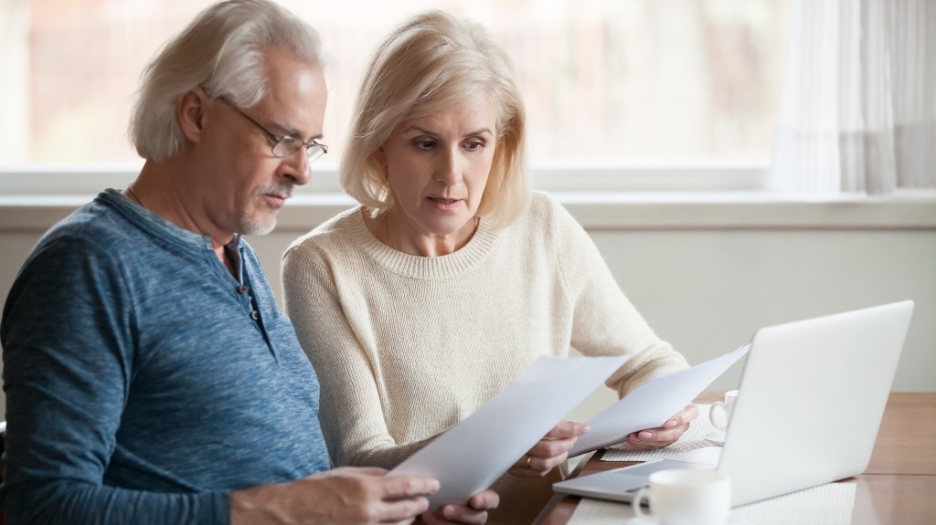 Old couple reviewing documents by a laptop
