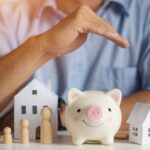 man holding hand over model of house, family and piggy bank_s