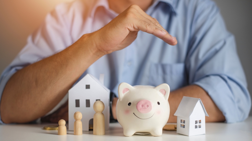 man holding hand over model of house, family and piggy bank