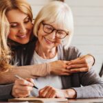 Adult daughter helping senior woman complete form at home_s