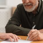 Notary showing senior man where to sign Last Will and Testament at wooden table indoors_s
