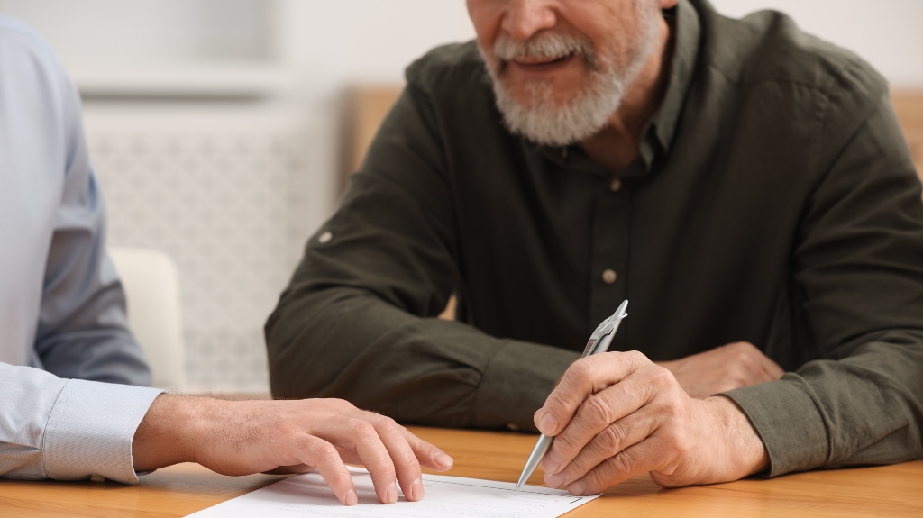 Notary showing senior man where to sign Last Will and Testament at wooden table indoors