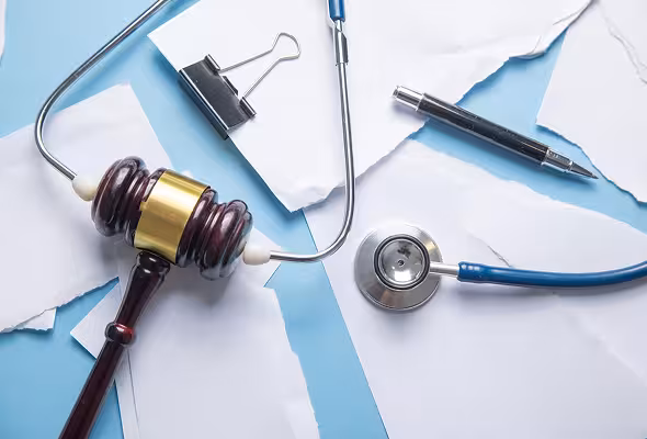 Wooden gavel, stethoscope, pen, and torn white papers on a blue surface.