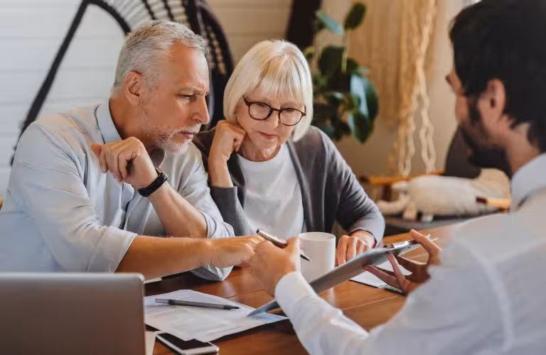 Three adults engaged in a discussion over documents at a wooden table in an office.