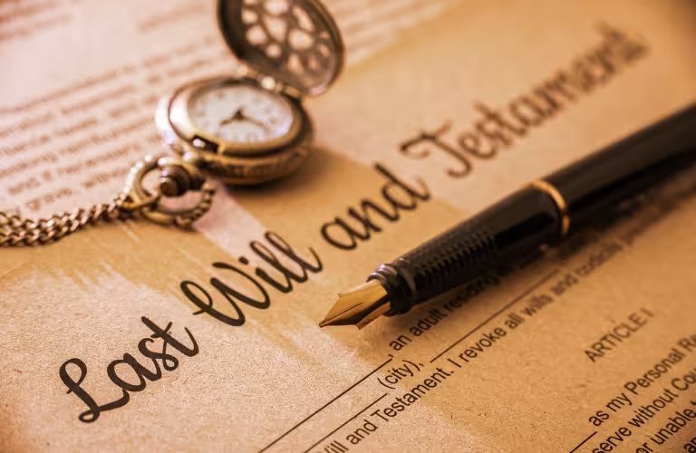 Close-up of a vintage pocket watch and fountain pen on a Last Will and Testament document.
