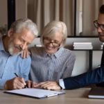 An older couple sits with a lawyer while reviewing and signing legal documents_s